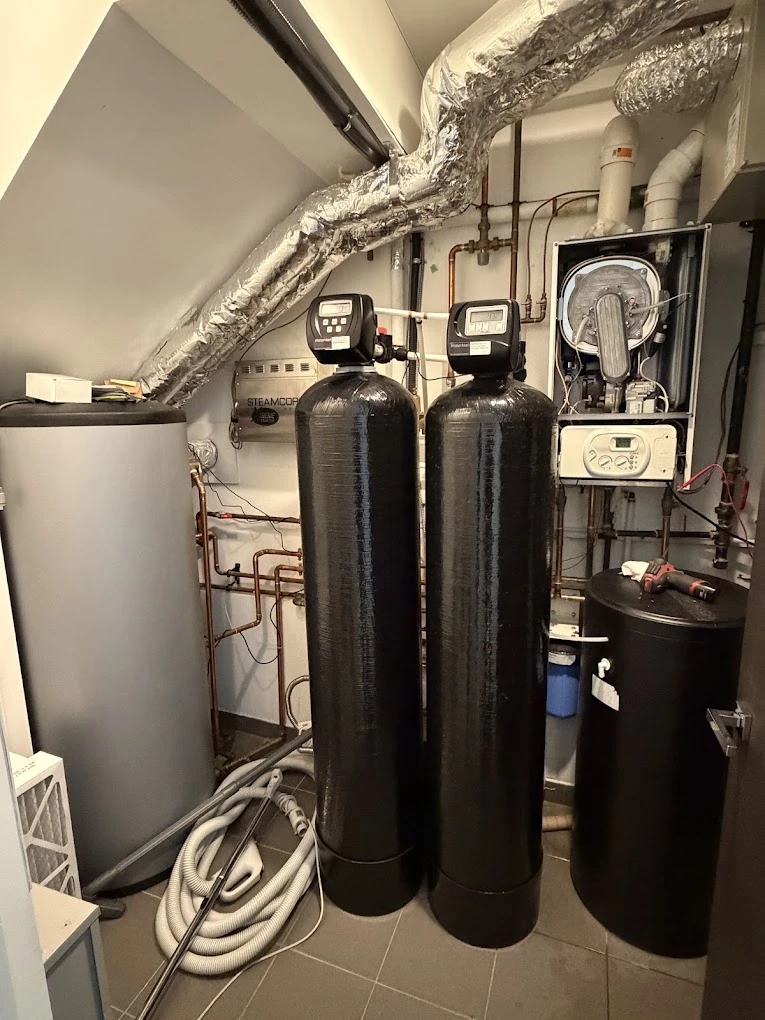 Mechanical room with twin water softeners, a wall-mounted boiler and insulated ducting.