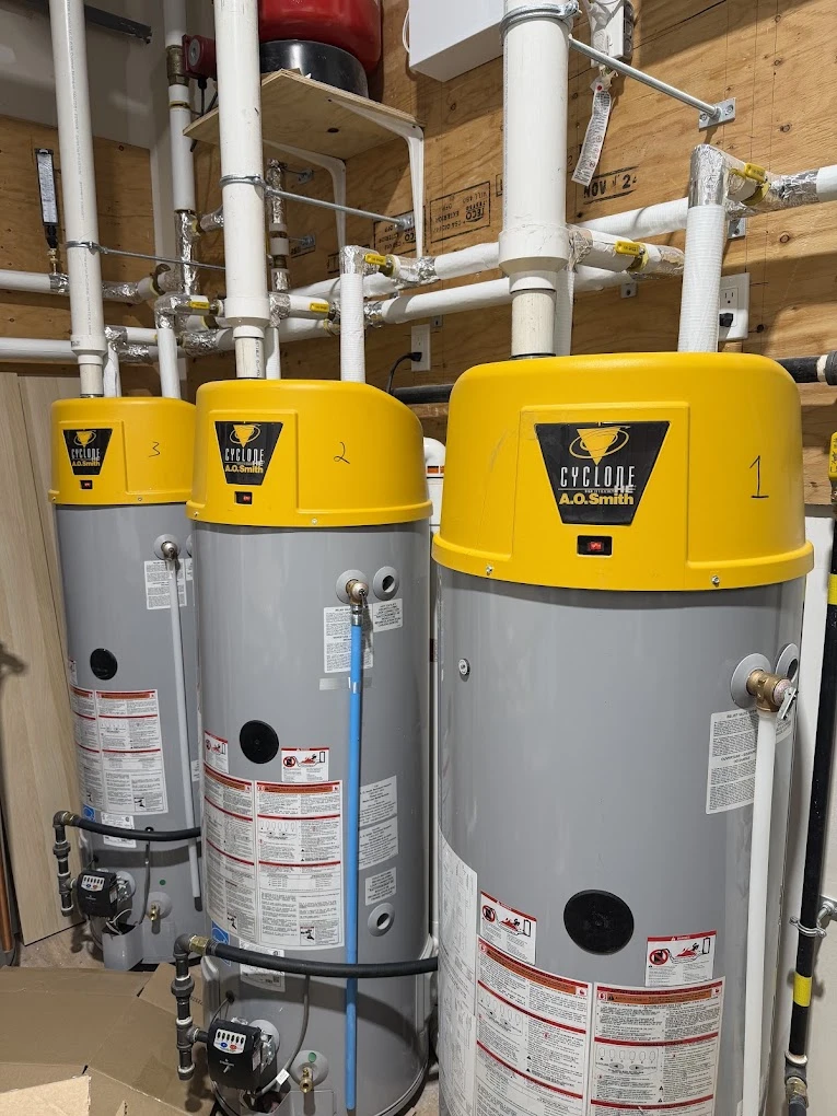Three commercial water heaters installed side by side in a plant room.